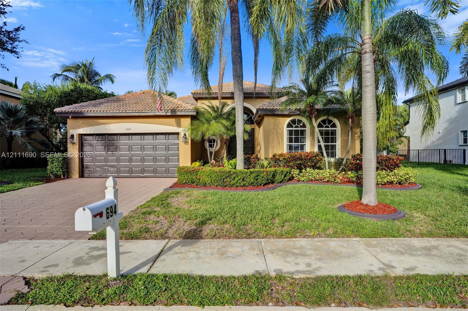 Single-story exterior featuring a tile roof, stucco finish, arched windows, and a paved driveway leading to a two-car garage Single-story exterior featuring a tile roof, stucco finish, arched windows, and a paved driveway leading to a two-car garage