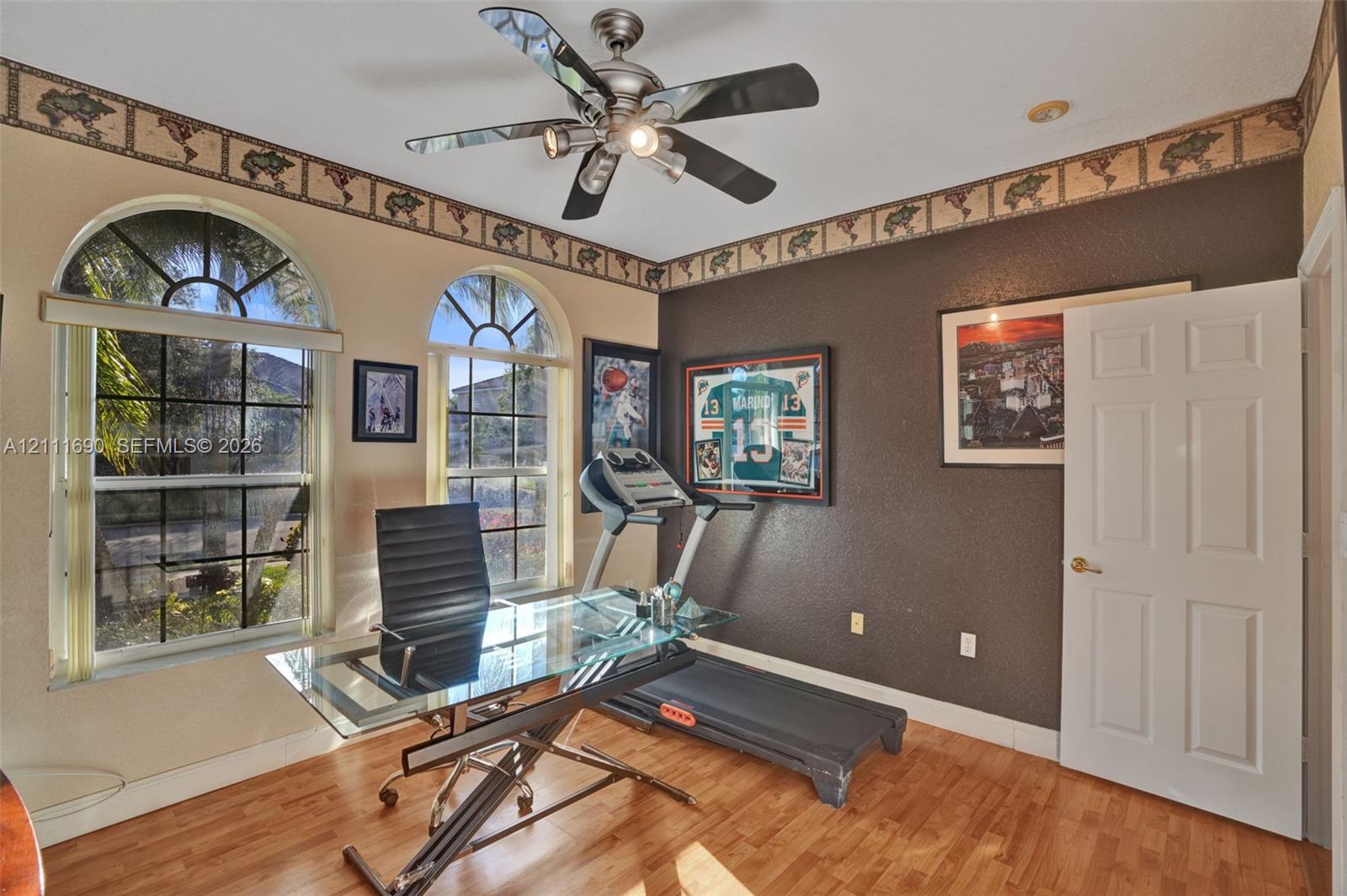 Room featuring arched windows, wood-finish flooring, and a ceiling fan with integrated lighting