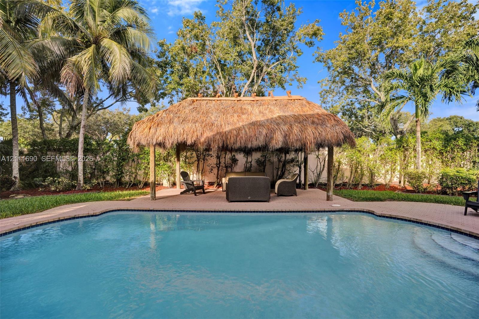 In-ground swimming pool with paver decking and a thatched-roof tiki hut