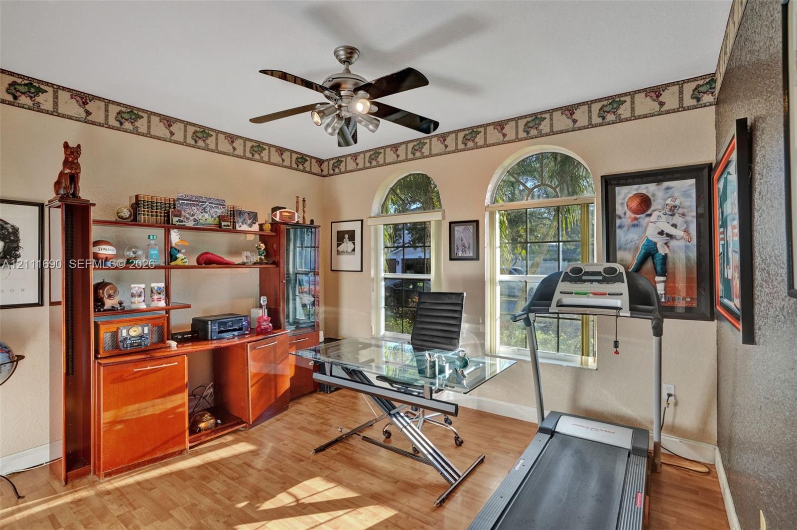 Room featuring wood-finish flooring, dual arched windows, and a ceiling fan with integrated lighting