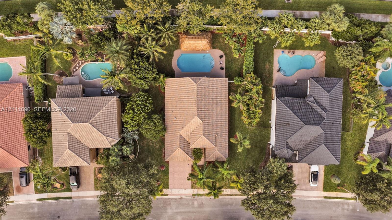 Aerial perspective featuring a shingle-roofed residence, a private swimming pool, paved driveway, and mature landscaping