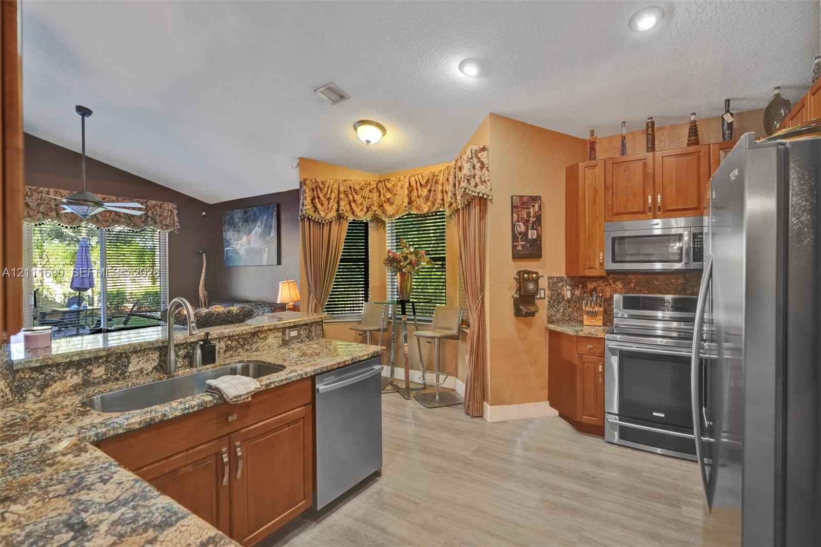 Kitchen featuring stone countertops, stainless steel appliances, wood cabinetry, recessed lighting, and a bay window