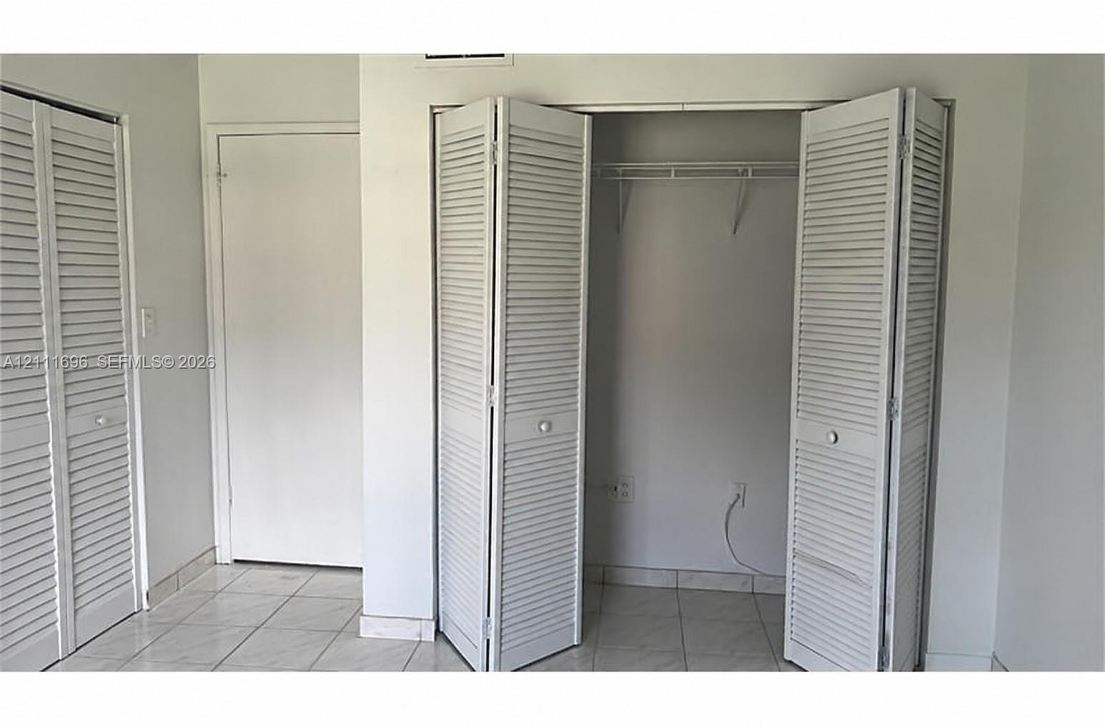 White louvered bifold closet doors, interior wall-mounted shelving, and light-toned tile flooring
