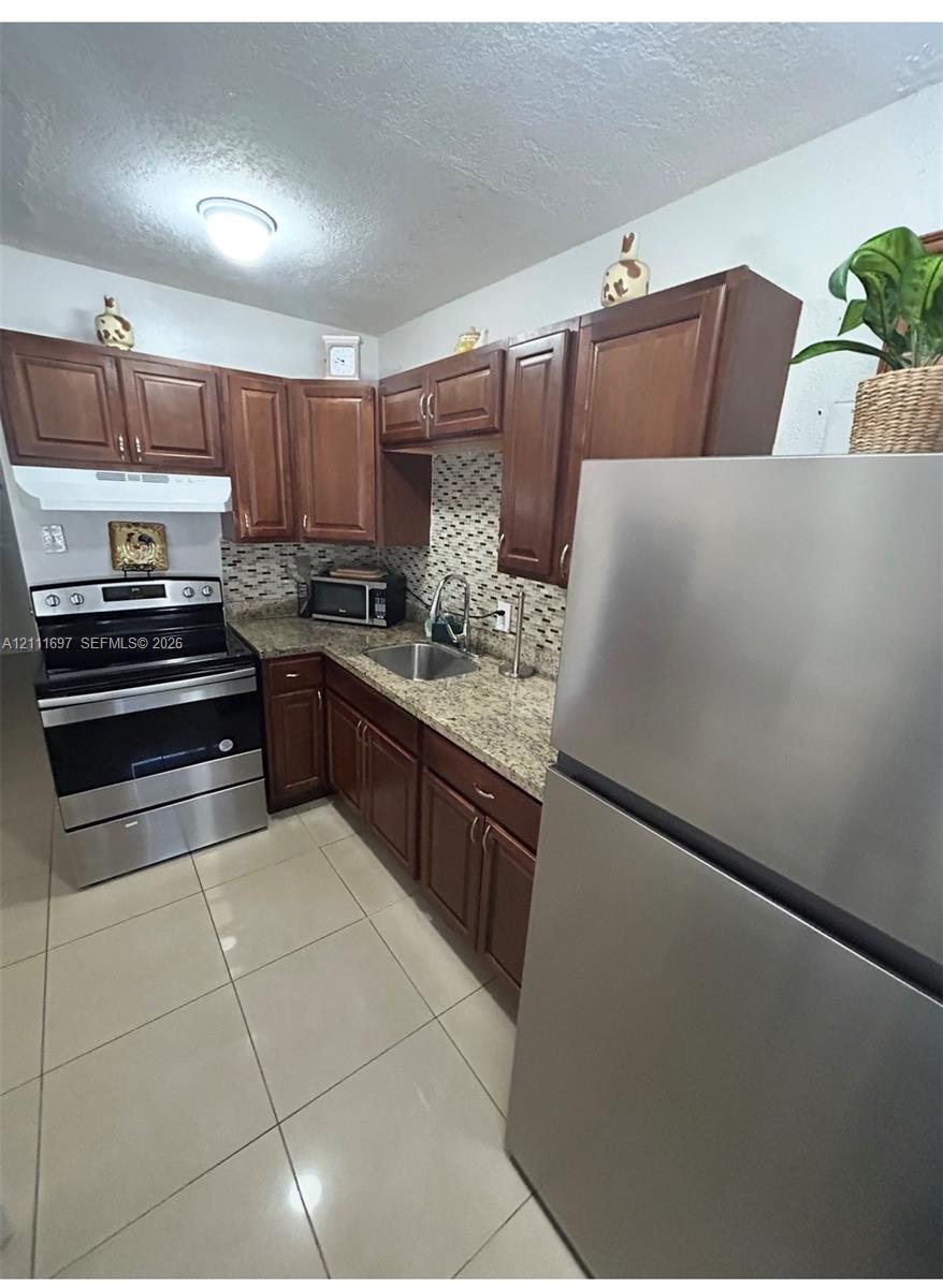 Kitchen featuring raised-panel wood cabinetry, stone-finish countertops, tile backsplash, tile flooring, and stainless steel appliances
