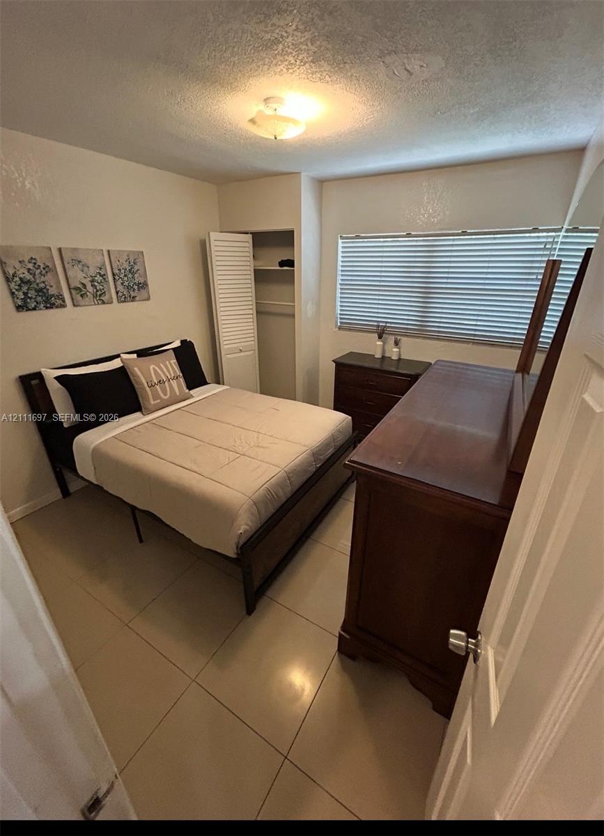 Ceramic tile flooring, neutral wall tones, window blinds, closet with louvered door, and overhead lighting