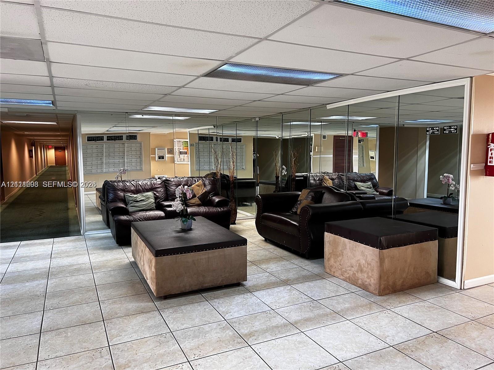 Common area featuring light-toned floor tiling, expansive floor-to-ceiling mirrored walls, and recessed grid ceiling lighting
