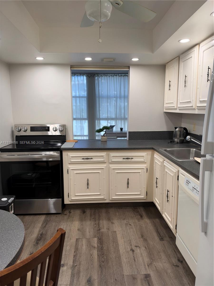 Kitchen featuring recessed lighting, wood-finish flooring, dark solid-surface countertops, paneled cabinetry, and stainless steel appliances