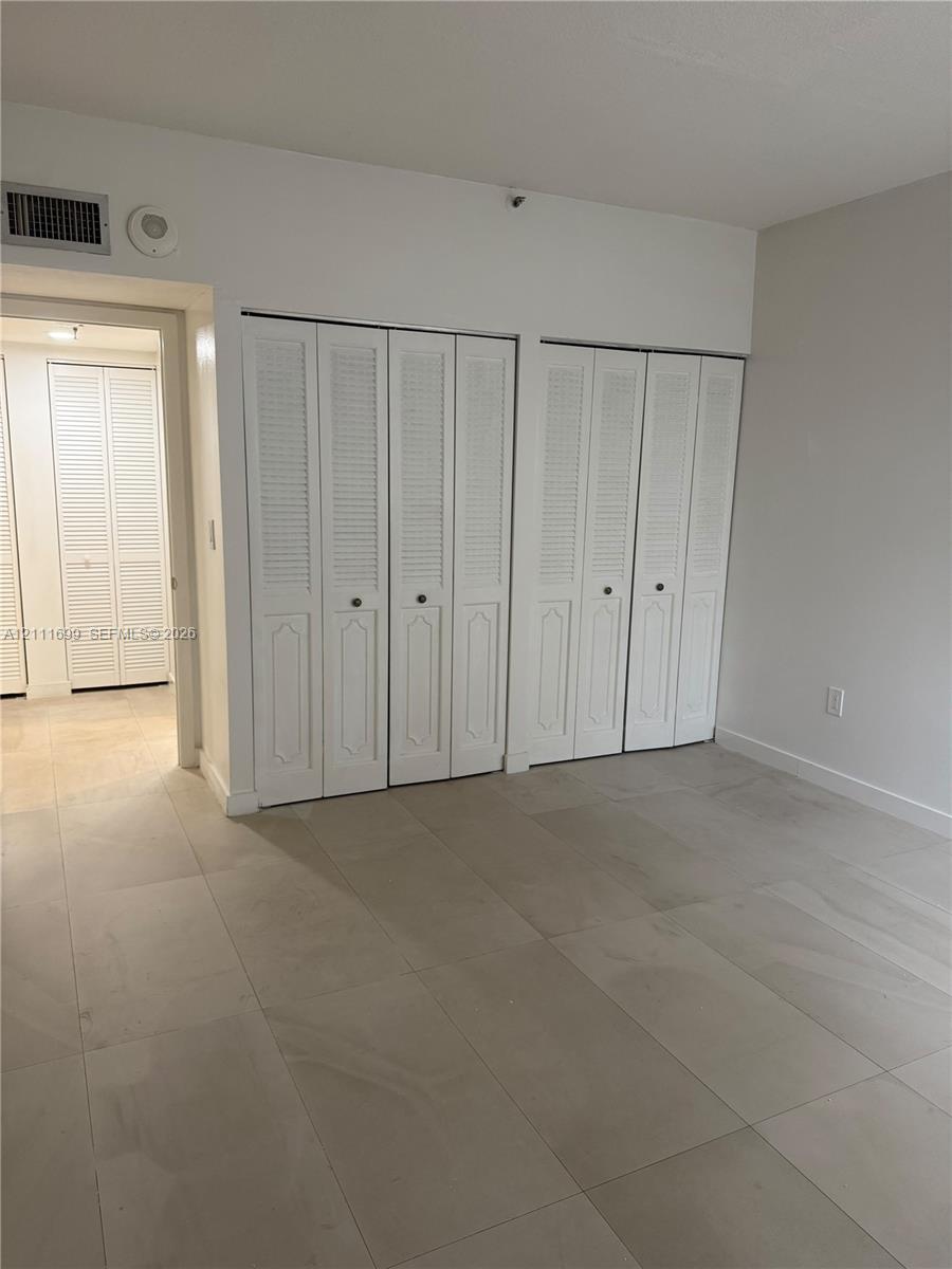 Interior space featuring neutral large-format tile flooring and dual sets of white louvered bi-fold closet doors