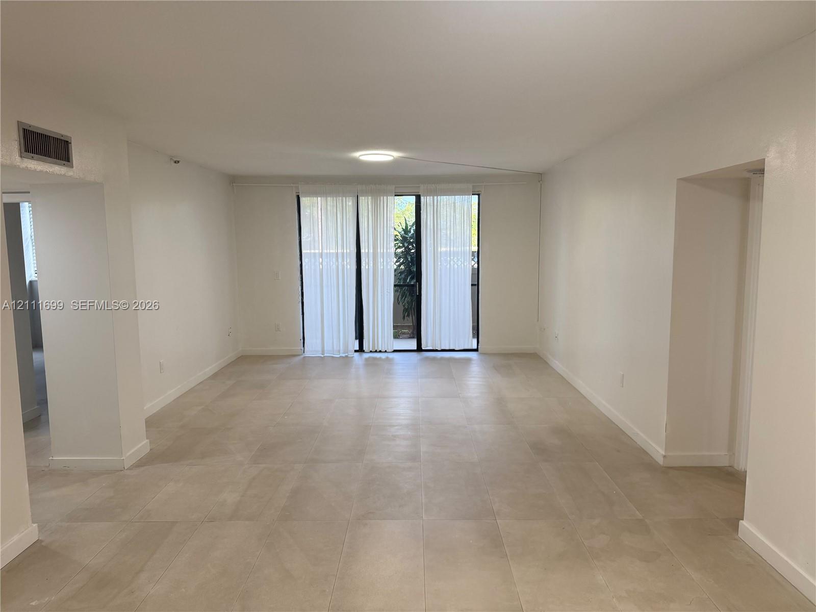 Open floor plan featuring large-format ceramic tile flooring, neutral walls, and a full-height glass sliding door with access to an exterior space