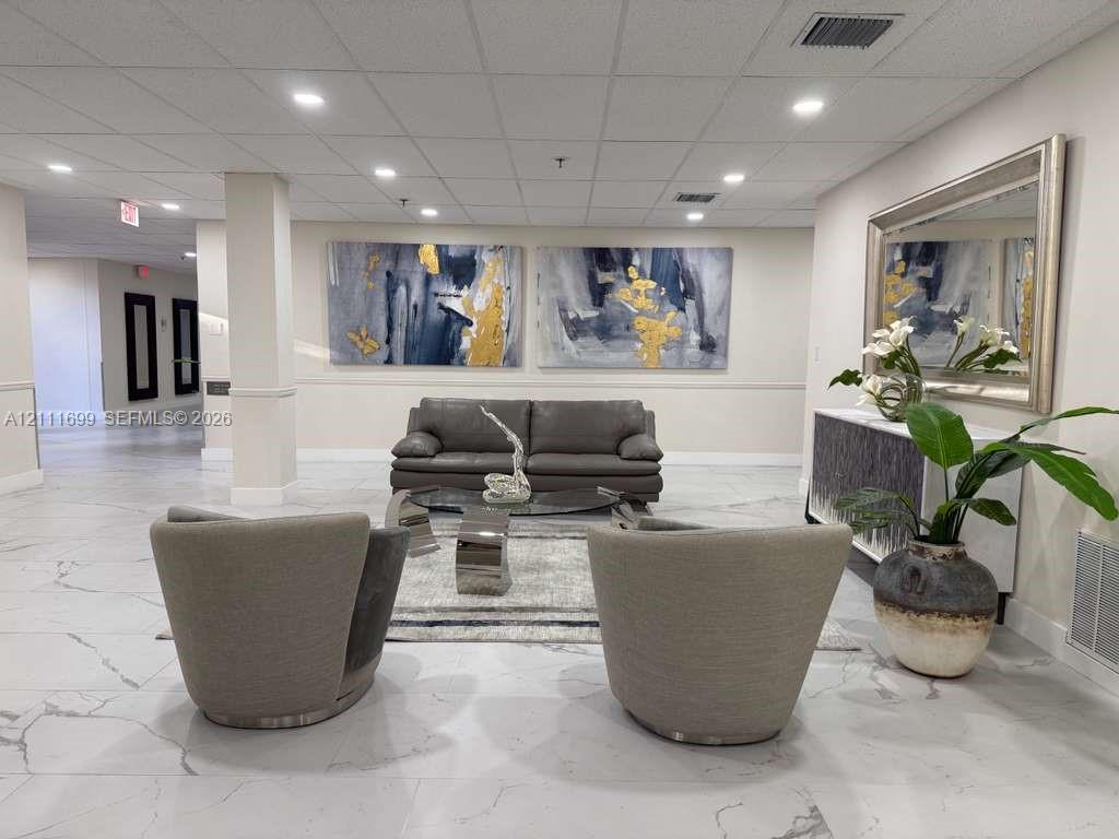 Spacious lobby area featuring large-format stone-patterned tile flooring, a suspended drop ceiling, and recessed lighting