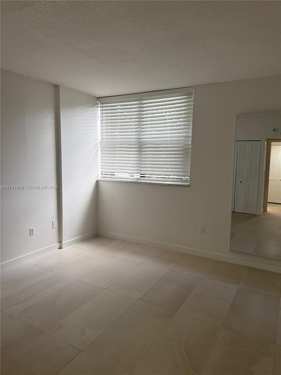 Neutral-toned tile flooring, large window with horizontal blinds, and mirrored closet doors