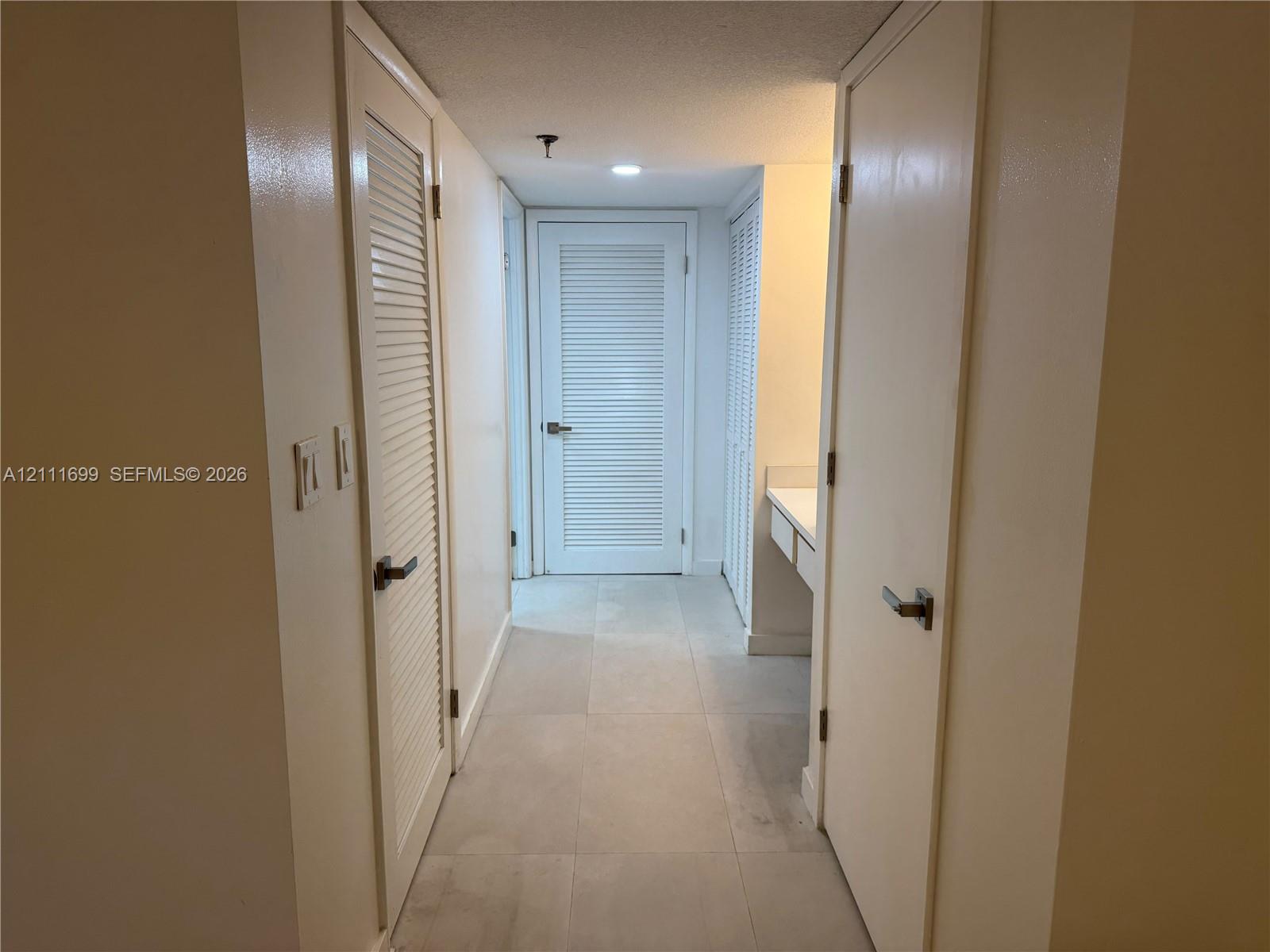 Hallway featuring large-format tile flooring, multiple white louvered doors, and built-in vanity cabinetry