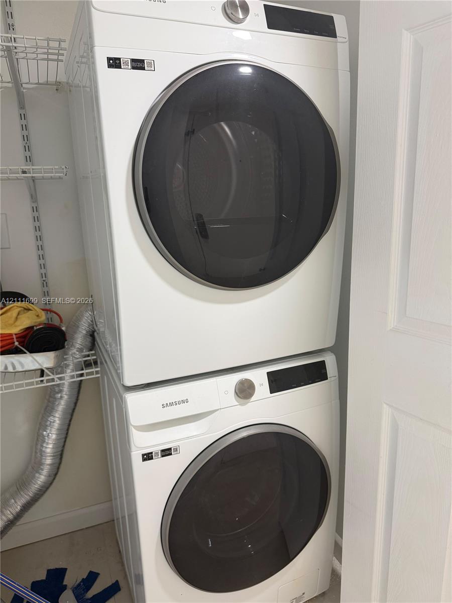 Stacked white front-load washer and dryer unit with metallic circular doors and built-in wire shelving