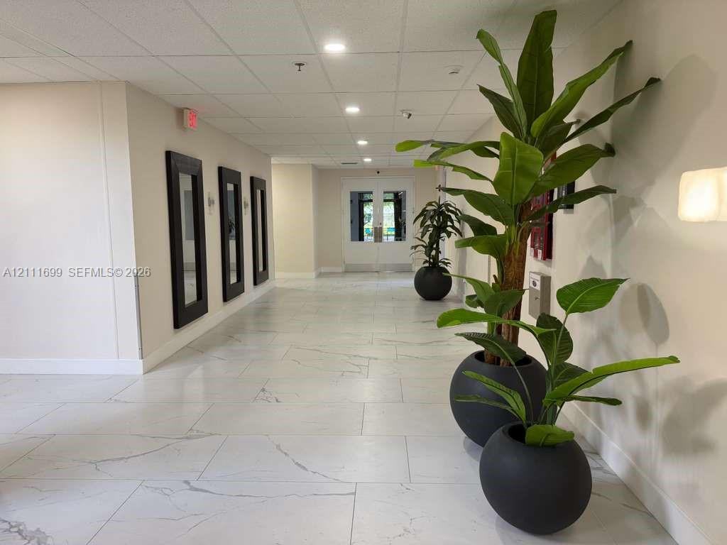 Wide hallway featuring large-format veined tile flooring, recessed ceiling lighting, and three wall-mounted decorative frames