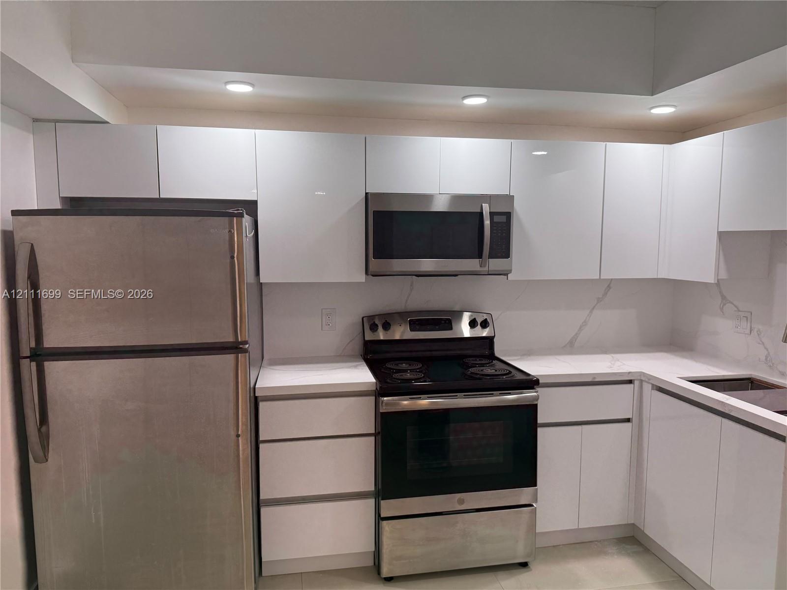 Kitchen featuring high-gloss white cabinetry, stone-finish countertops with veining, stainless steel appliances, recessed ceiling lighting, and tile flooring