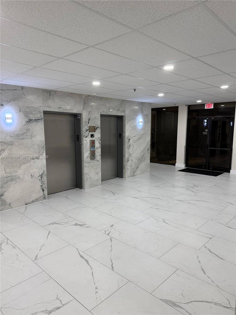 Elevator lobby featuring stone-paneled walls, large-format tiled flooring, recessed ceiling lighting, and dual metallic elevator doors