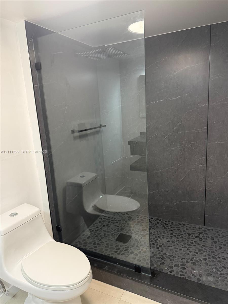Walk-in shower featuring a frameless glass enclosure, floor-to-ceiling stone-patterned tile surround, pebble-style stone flooring, and a recessed shower head
