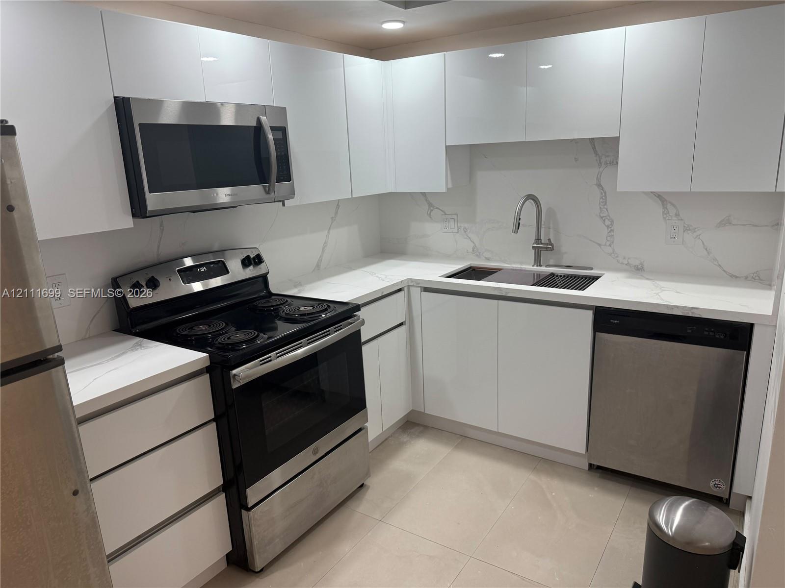 Kitchen featuring high-gloss white cabinetry, stone-surface countertops with backsplash, stainless steel appliances, and a pull-down kitchen faucet