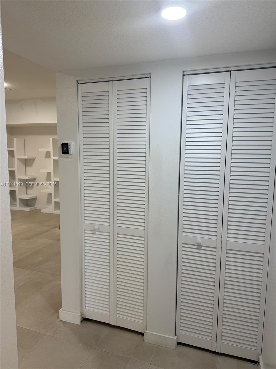 Dual white bi-fold louvered closet doors, neutral tile flooring, and integrated white open-shelf wall cabinetry
