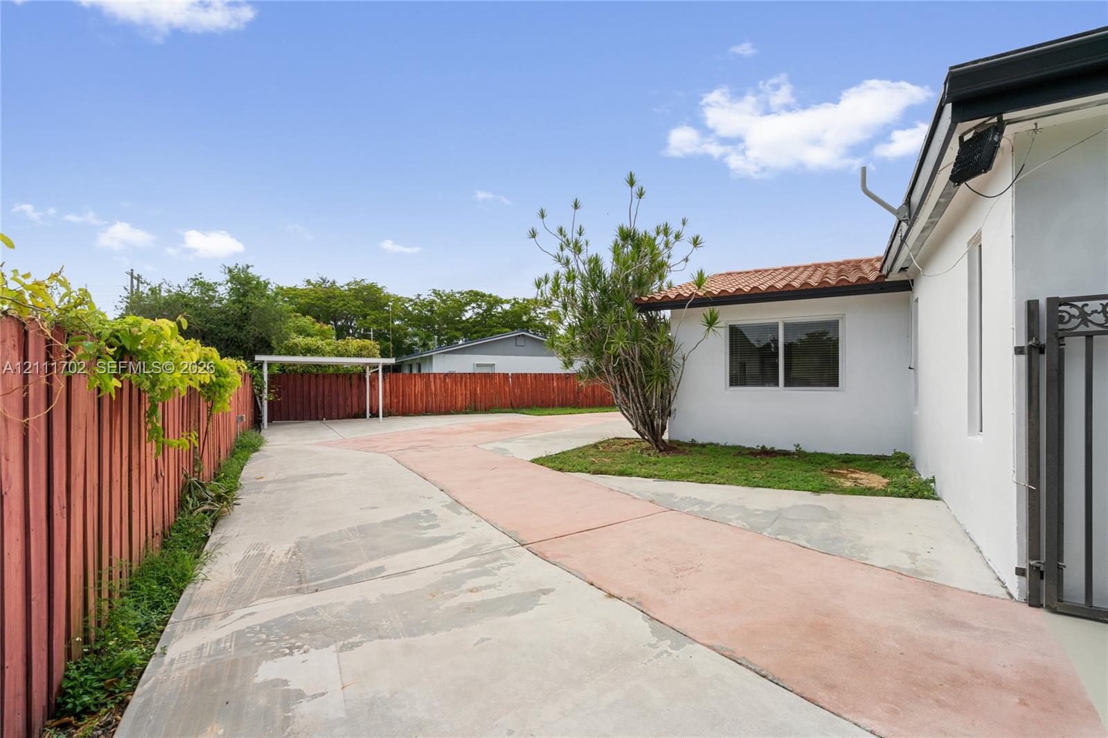 Exterior space featuring a concrete driveway, covered parking structure, fenced perimeter, and low-maintenance landscape elements