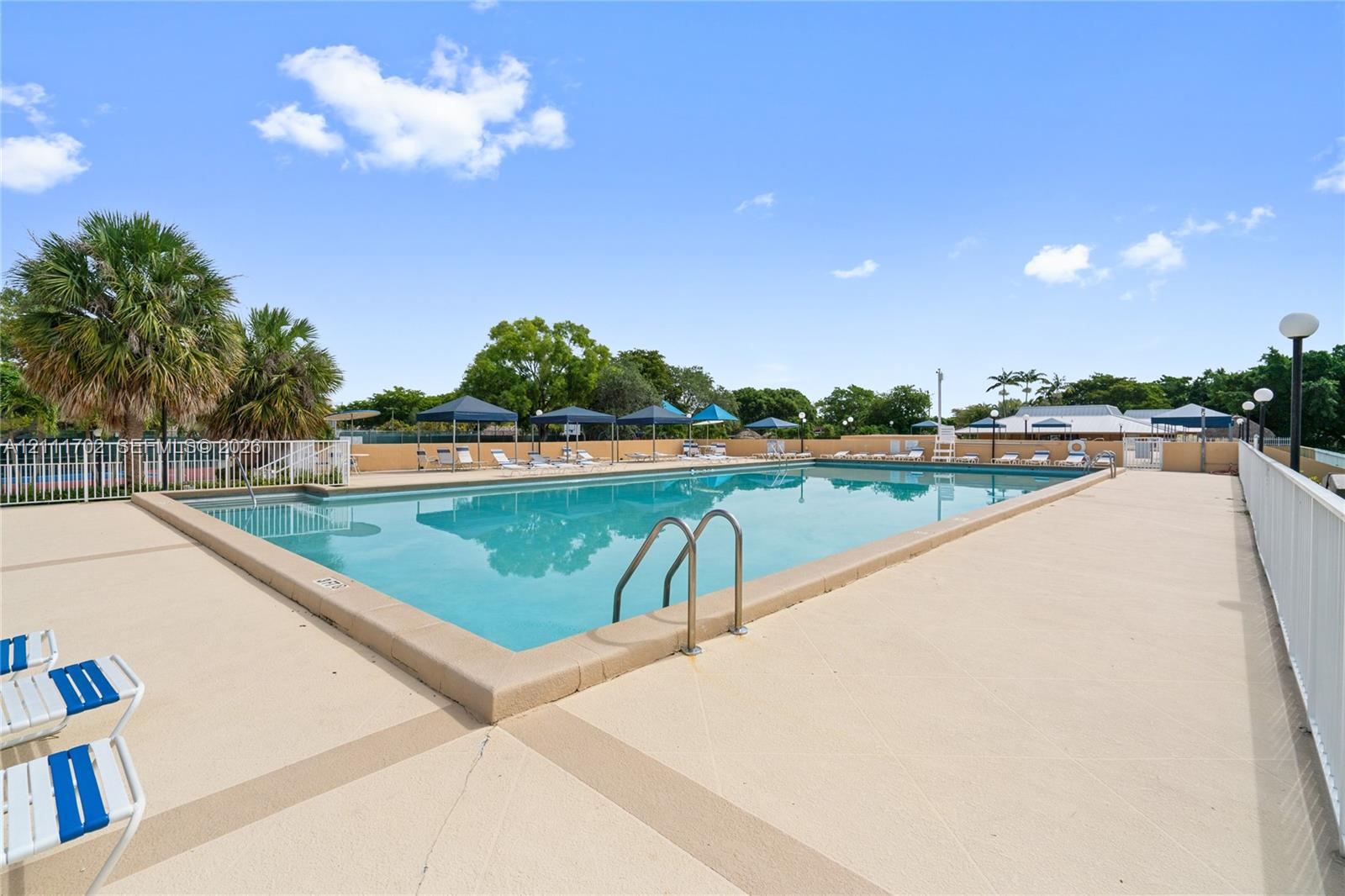 Rectangular in-ground swimming pool featuring a concrete deck, metal pool ladder, and white perimeter fencing