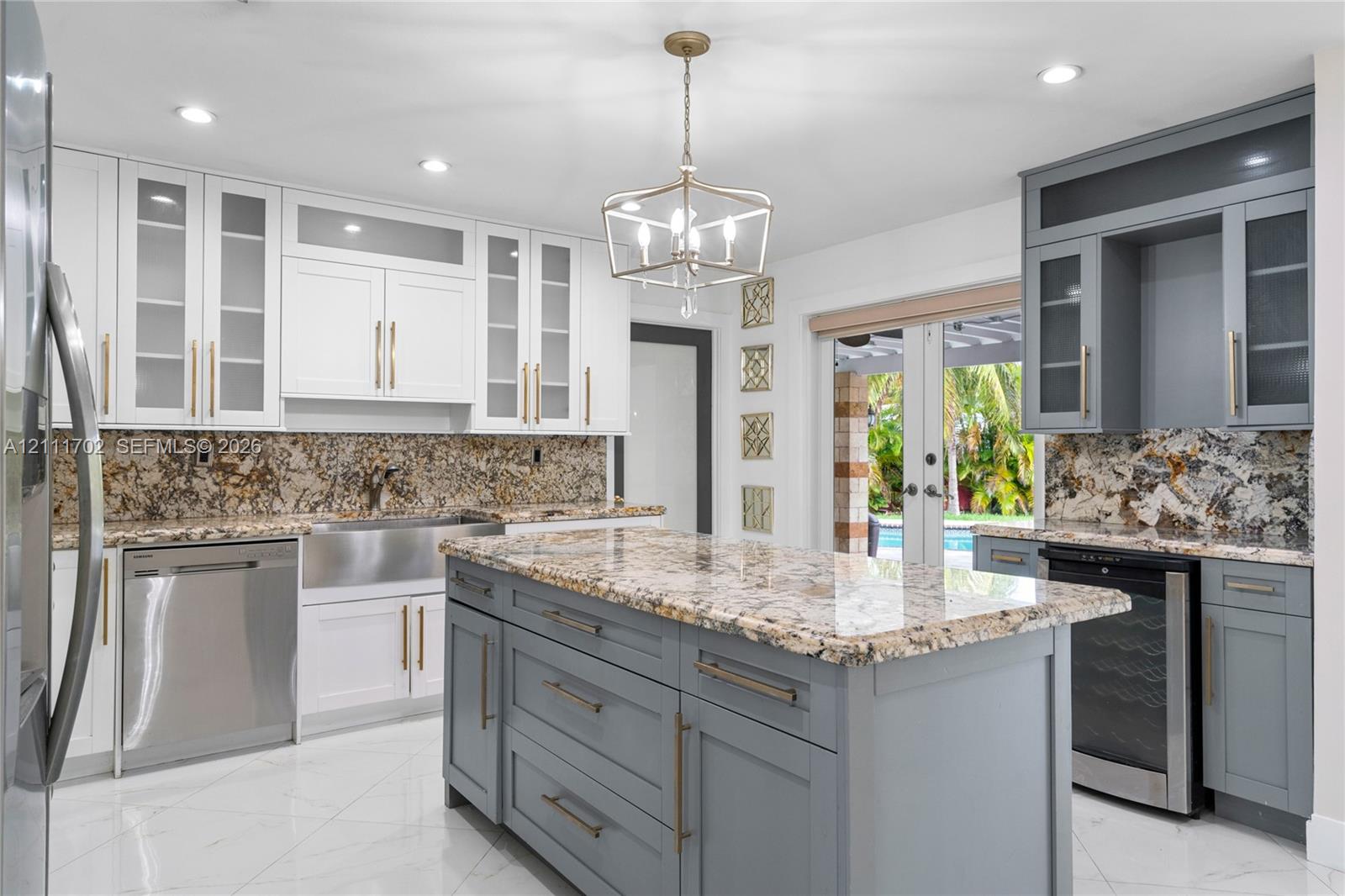 Kitchen featuring two-tone cabinetry with glass-front uppers, a central island with storage, stone countertops, a stainless steel apron-front sink, and large-format tile flooring