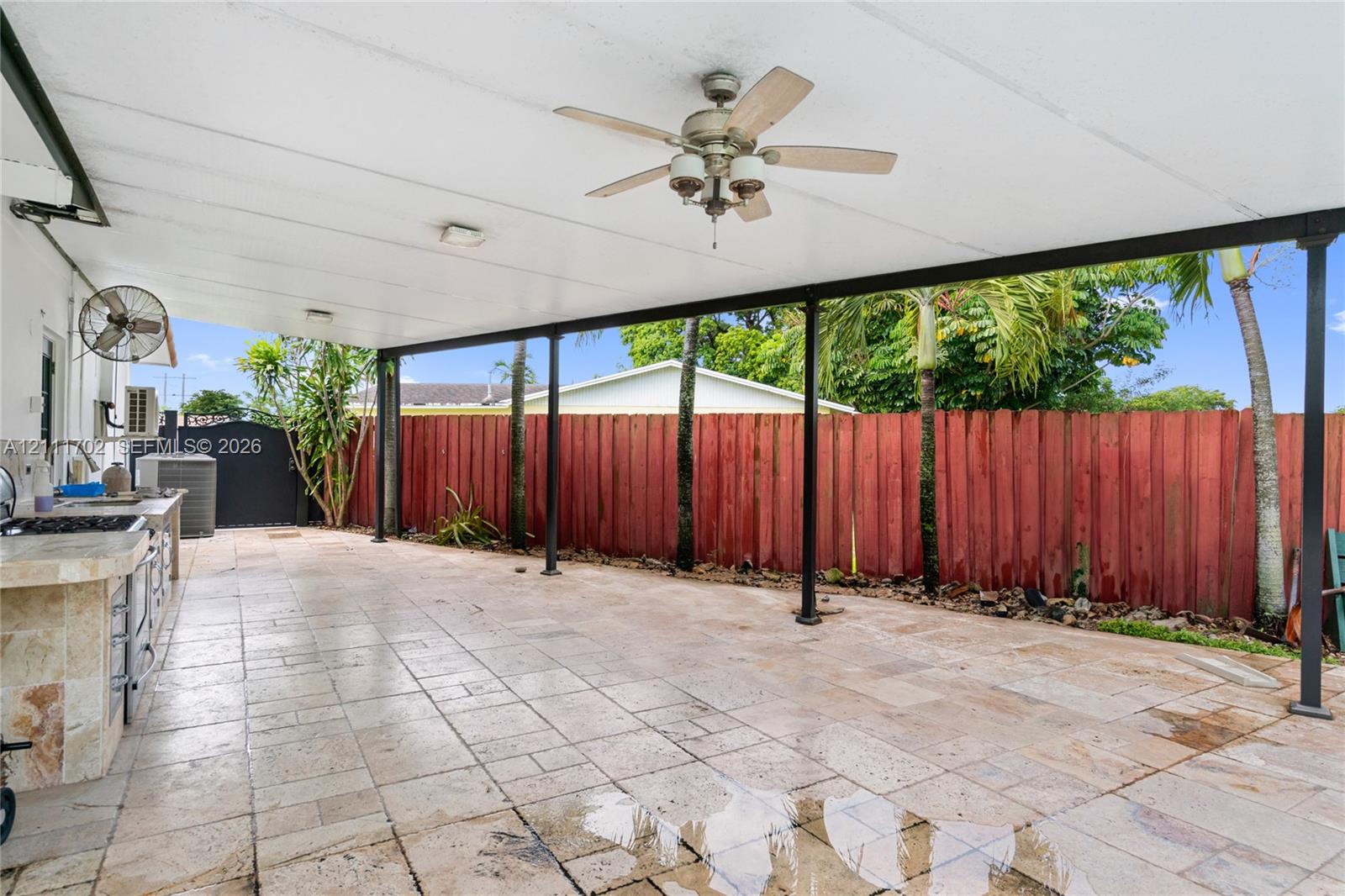 Covered patio featuring stone-tile flooring, built-in outdoor kitchen with stone finish, ceiling fan, and privacy fencing
