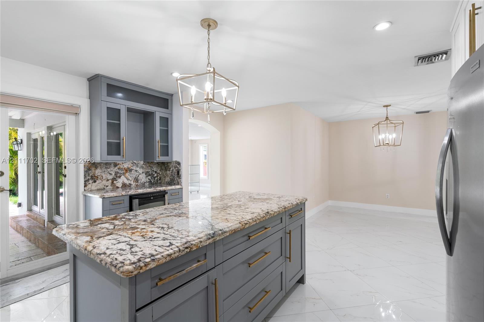 Kitchen island with stone countertop, gray shaker-style cabinetry, metallic pendant lighting, and polished flooring Kitchen island with stone countertop, gray shaker-style cabinetry, metallic pendant lighting, and polished flooring