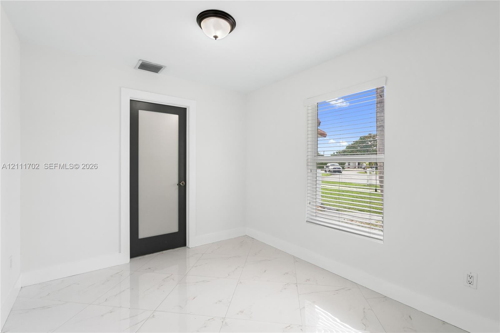 Neutral-toned interior featuring large-format tile flooring, a dark-framed interior door with a frosted glass pane, and a flush-mount ceiling light fixture