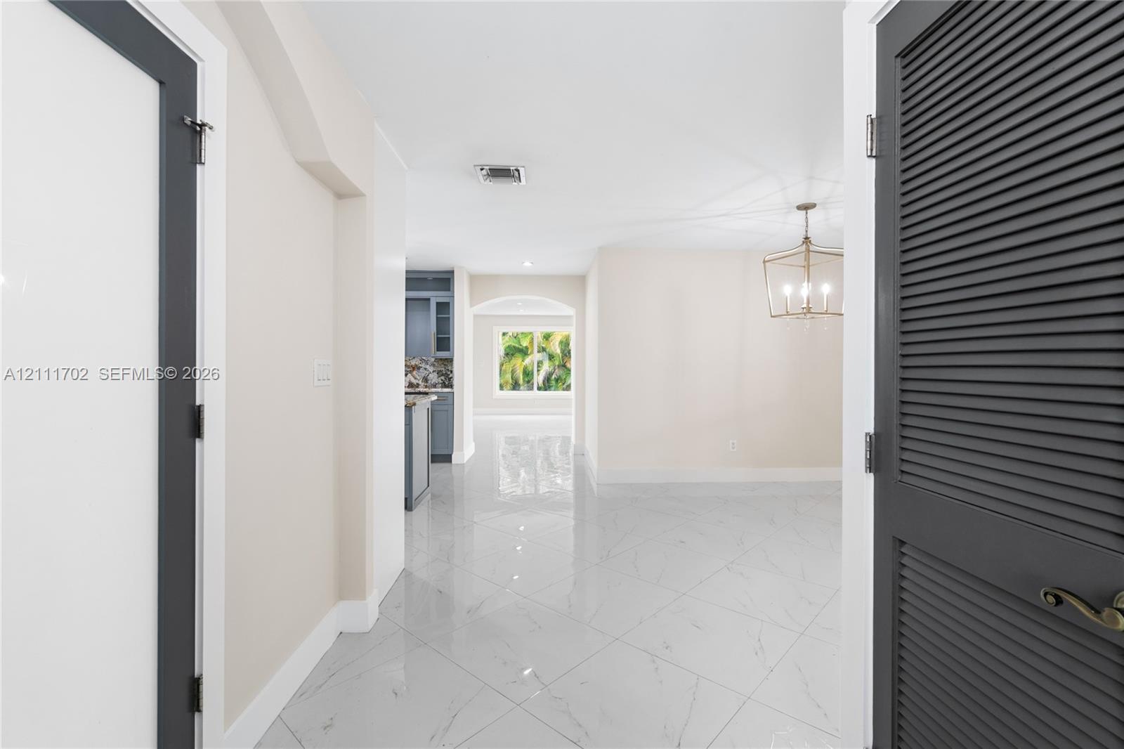Interior featuring polished tile flooring with a marble-patterned finish, dark gray louvered closet doors, and a geometric metal pendant light fixture