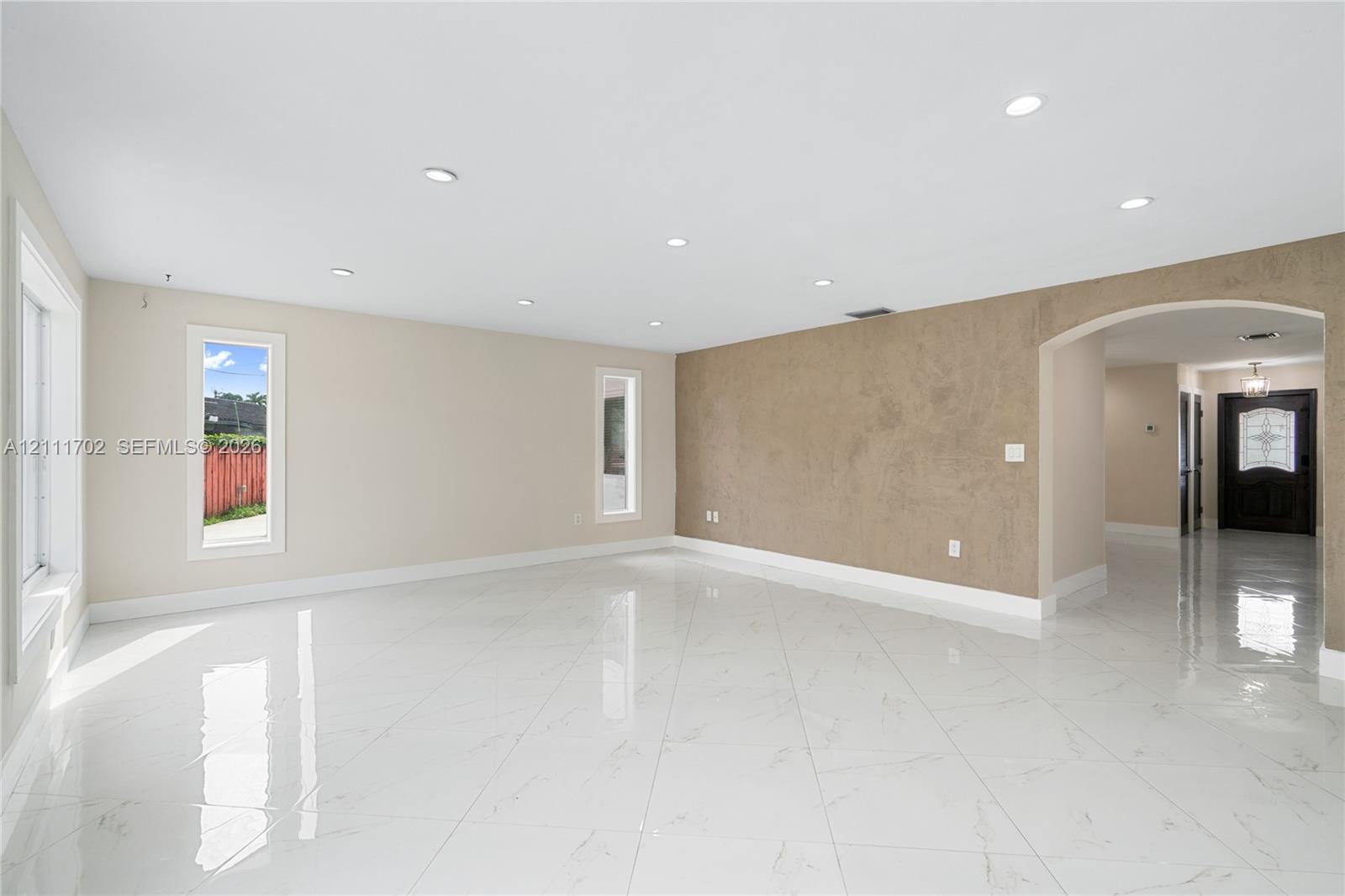 Open interior space featuring polished tile flooring, recessed lighting, a textured accent wall, and an arched entry