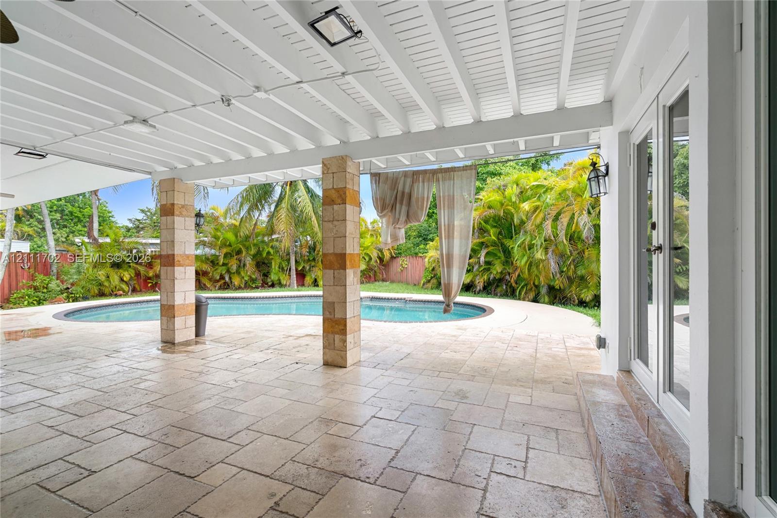 Covered patio featuring stone-tile flooring, vaulted beadboard ceiling, structural stone-clad columns, and a custom-shaped swimming pool Covered patio featuring stone-tile flooring, vaulted beadboard ceiling, structural stone-clad columns, and a custom-shaped swimming pool