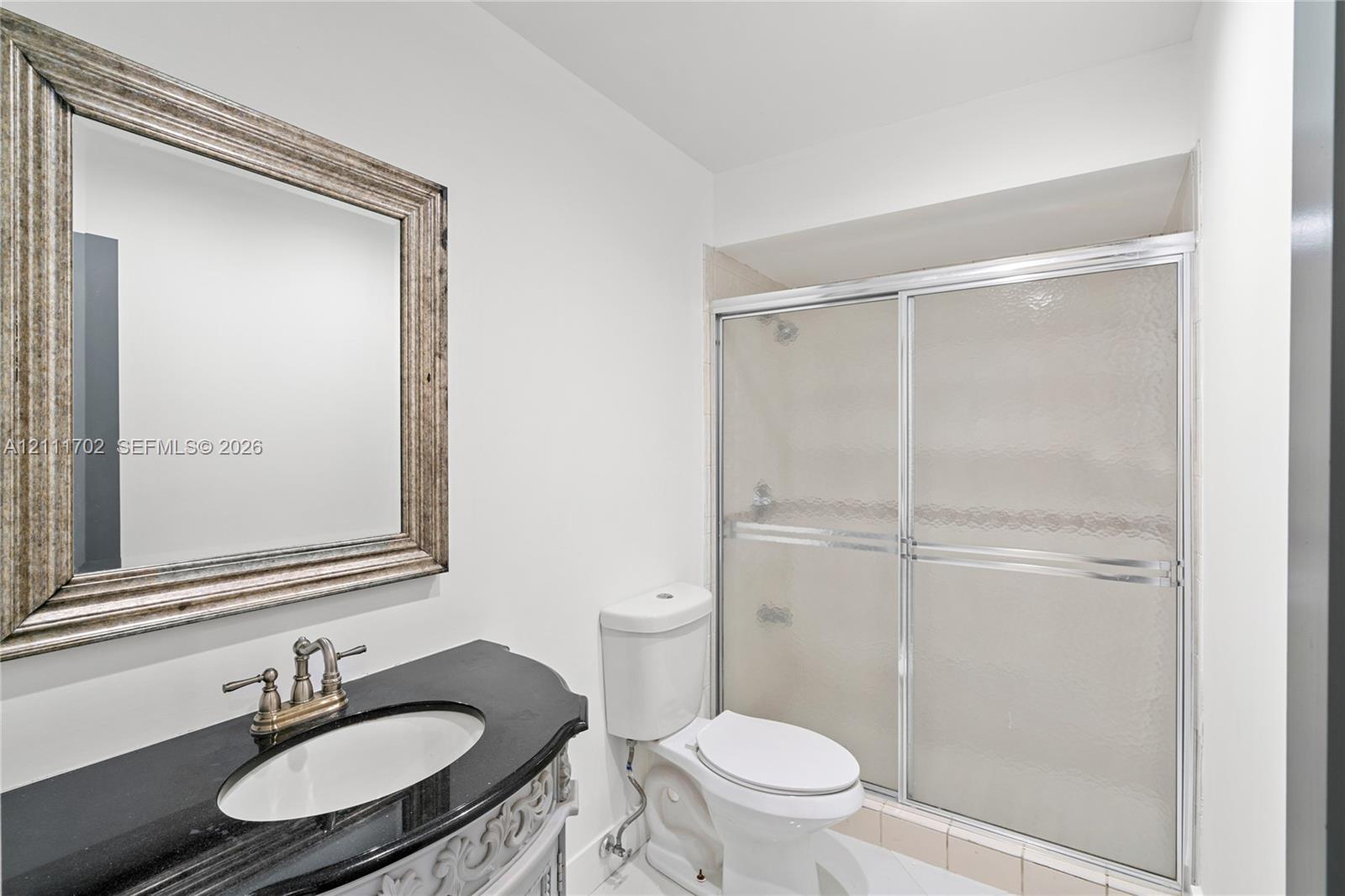 Bathroom featuring a vanity with a dark stone countertop, integrated oval sink, metallic widespread faucet, and a shower enclosure with sliding glass doors