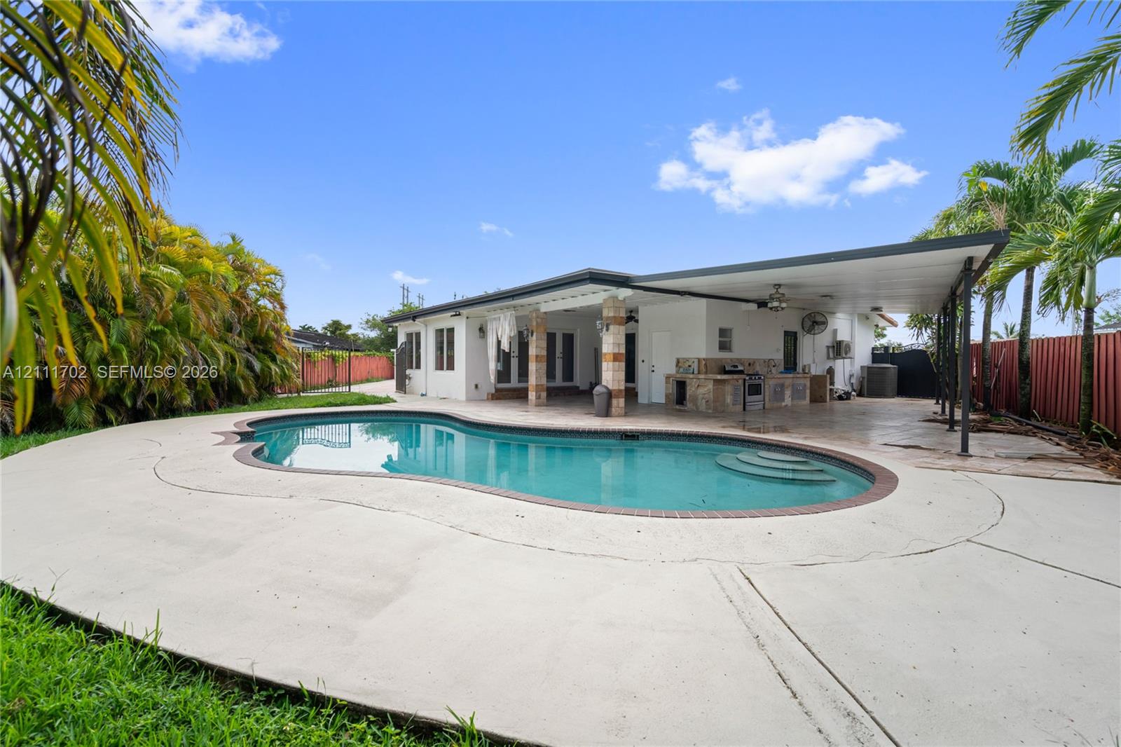 In-ground pool with brick coping, expansive concrete pool deck, covered outdoor patio, and built-in masonry grill station