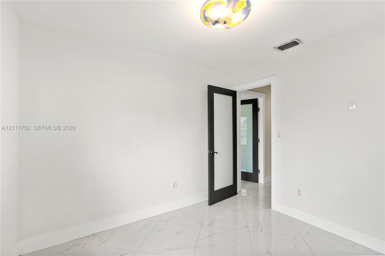 Interior space featuring polished stone-finish tile flooring, matte black doors with frosted glass panels, and a modern circular flush-mount ceiling light
