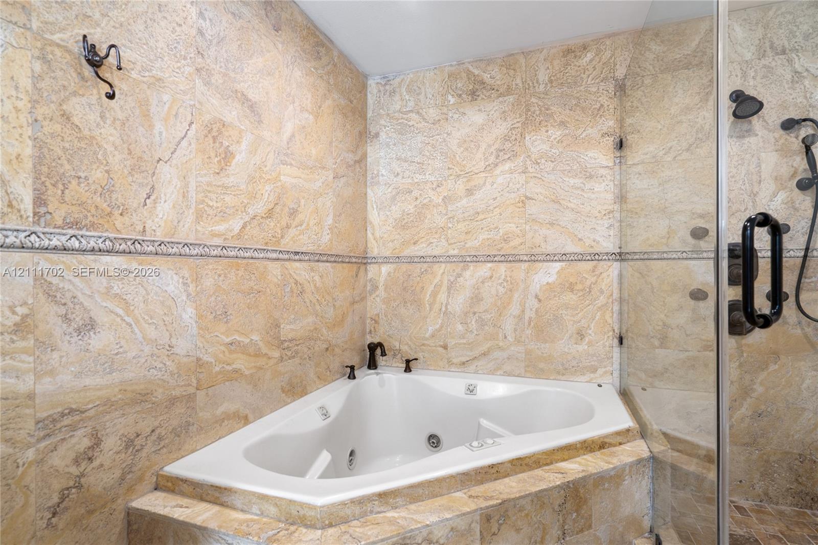 Corner soaking tub featuring stone tile surround, integrated decorative tile inlay, glass-enclosed shower, and oil-rubbed bronze fixtures