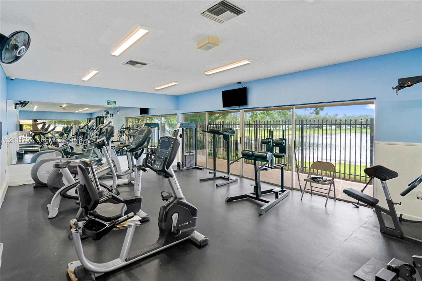 Fitness center featuring rubber flooring, expansive wall-to-wall mirrors, recessed lighting, and floor-to-ceiling glass sliding doors with exterior metal fencing