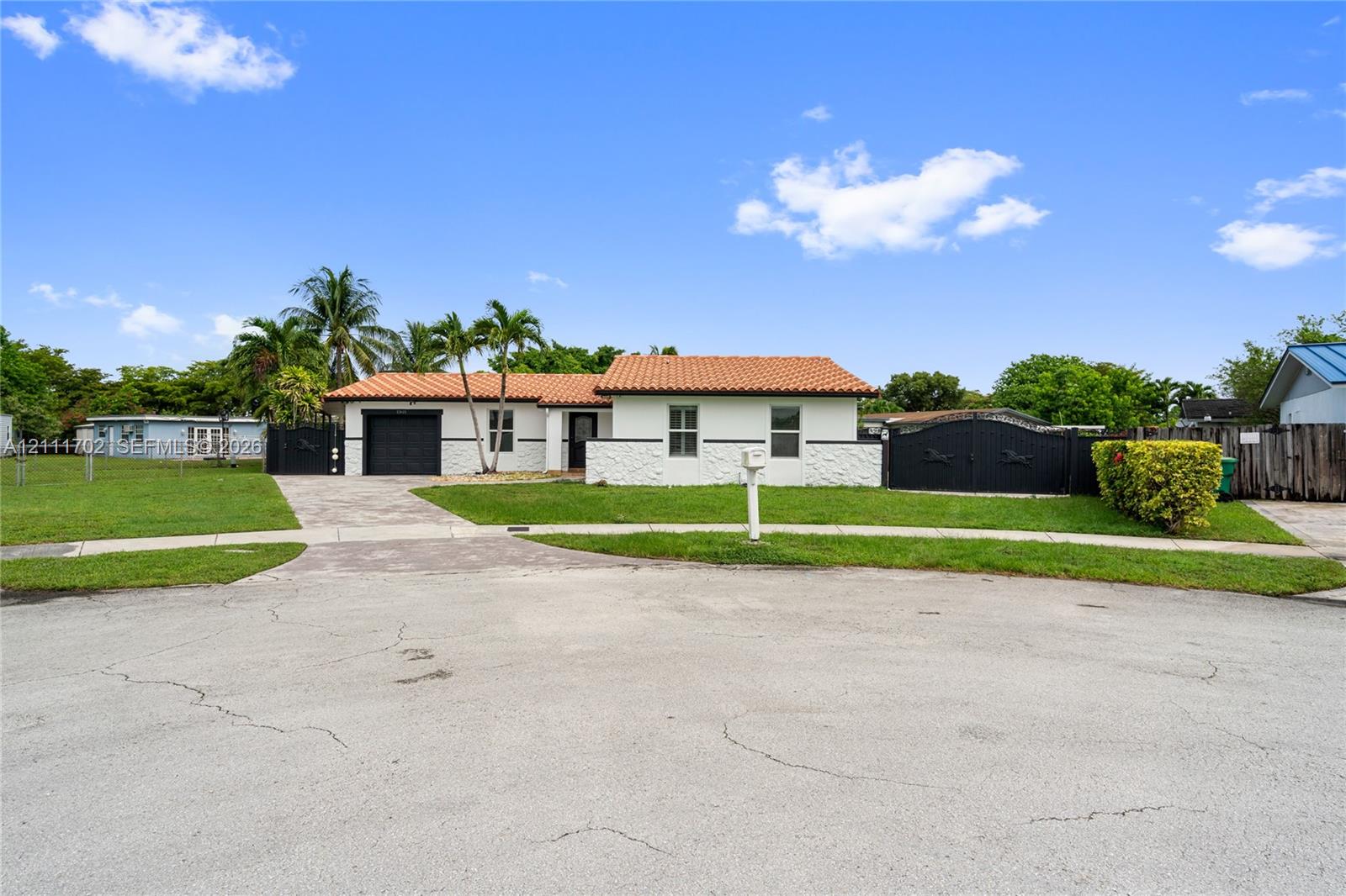 Single-story exterior featuring a clay tile roof, white stucco facade, decorative masonry accent wall, and expansive paved driveway