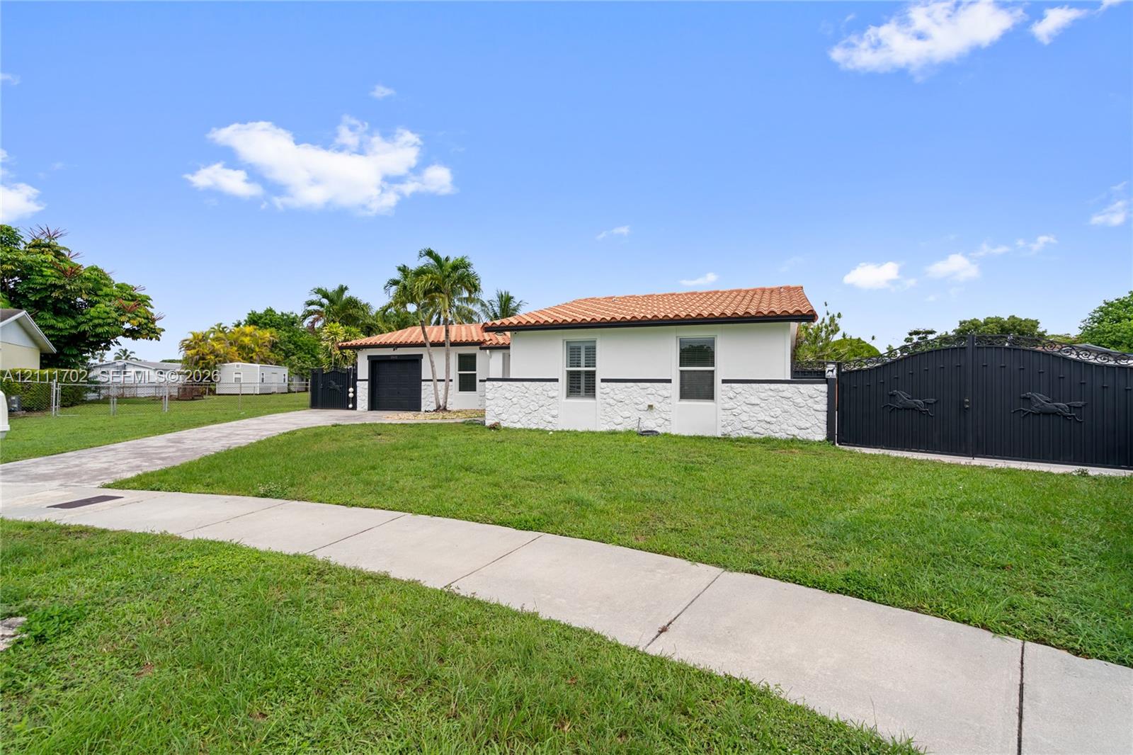 Single-story residence featuring a terracotta-tile roof, white stucco exterior with textured stone facade accents, an attached garage, and a gated entrance