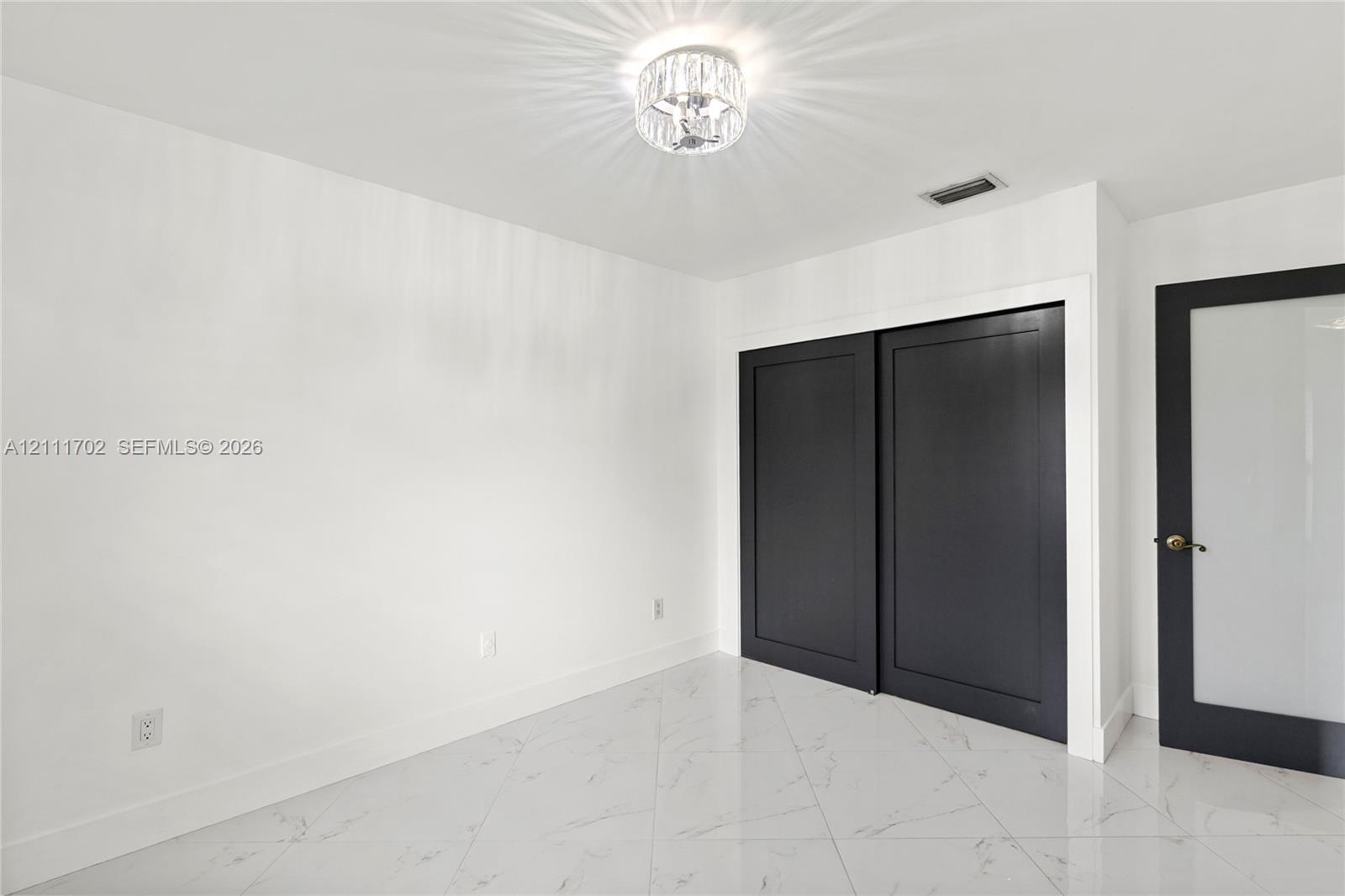 Polished stone-finish tile flooring, matte black sliding closet doors, decorative crystal-style flush mount ceiling lighting, and a solid-core door featuring a frosted glass panel