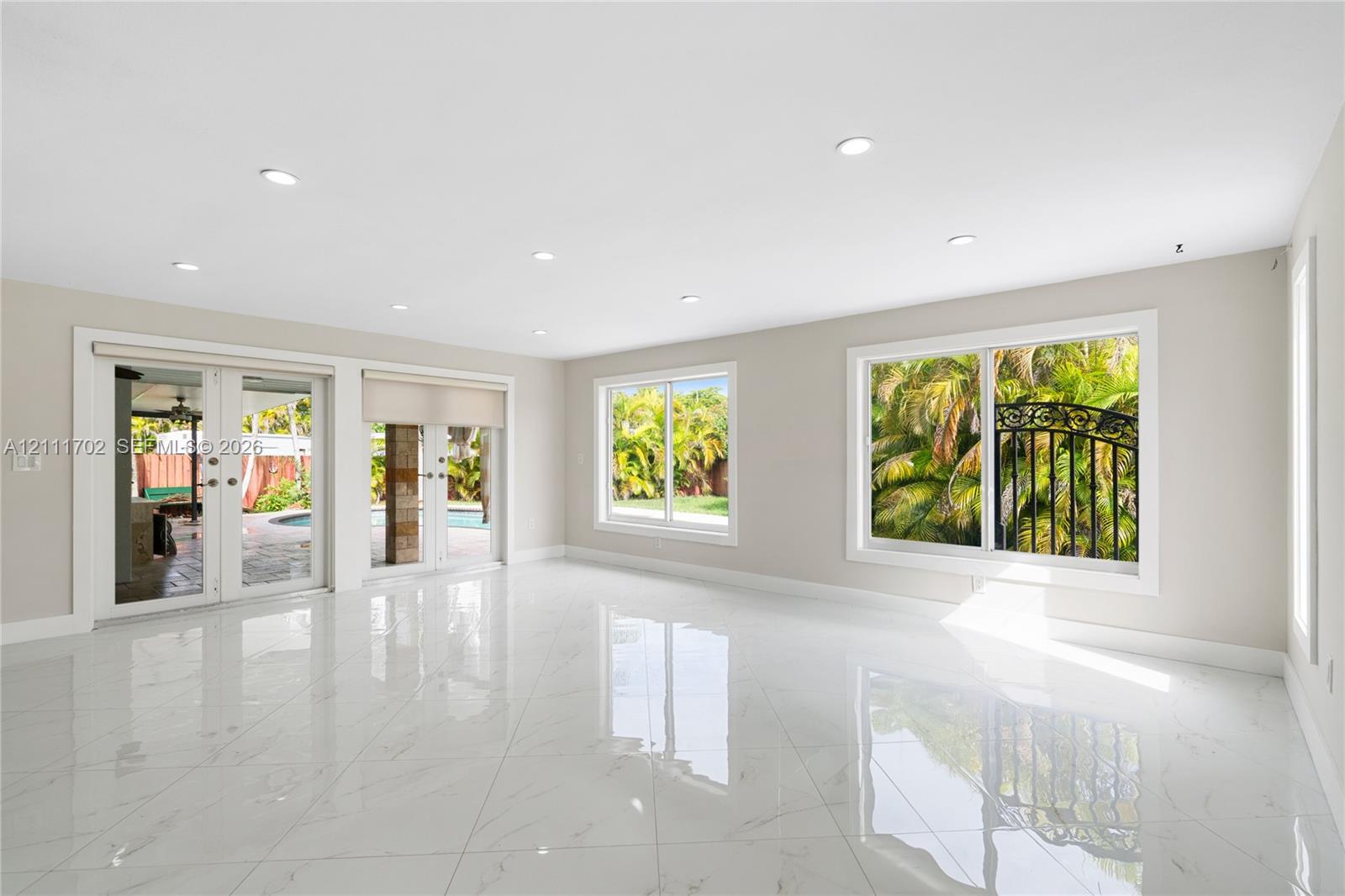 Open-concept interior featuring large-format polished stone-finish tile flooring, recessed ceiling lighting, dual sliding glass doors, and expansive picture windows