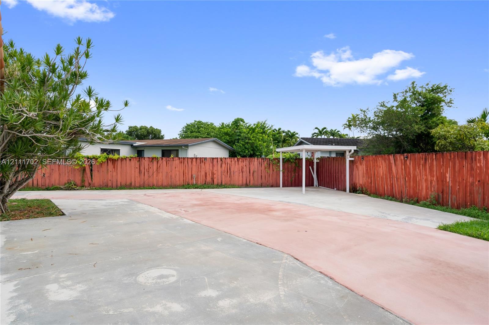 Expansive concrete surfacing, wood-plank perimeter fencing, and a detached metal-frame covered structure