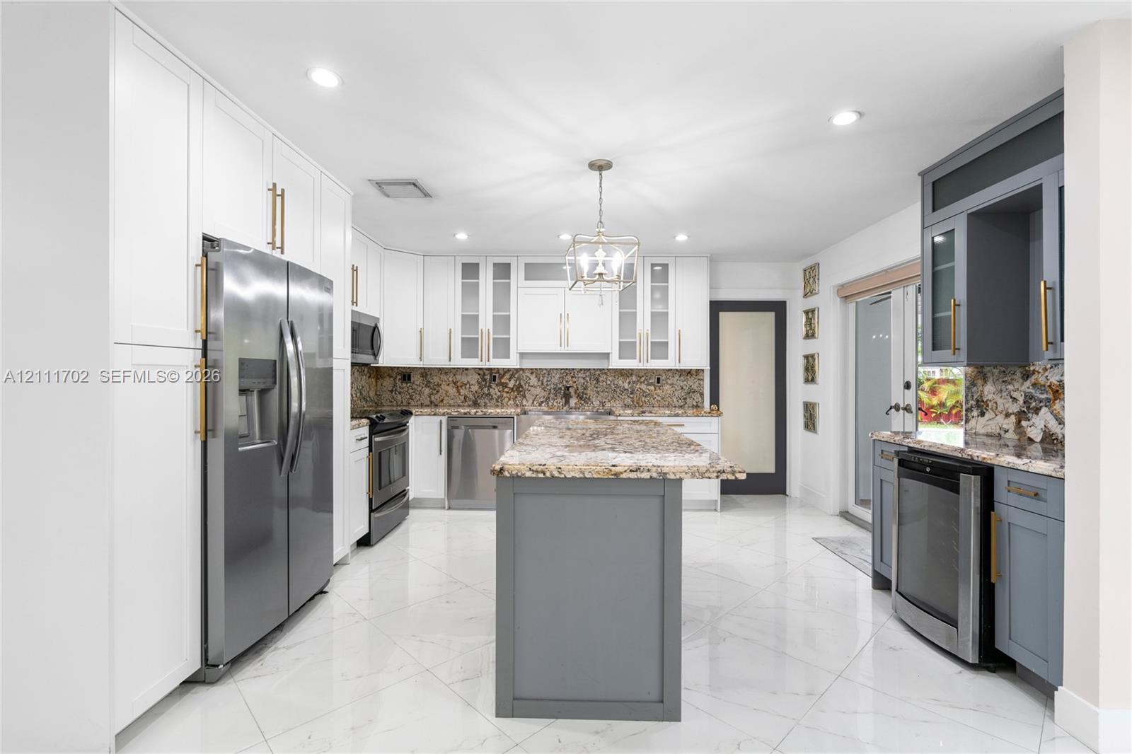 Kitchen featuring white and gray shaker-style cabinetry, stone countertops, central island, stainless steel appliances, and large-format tile flooring