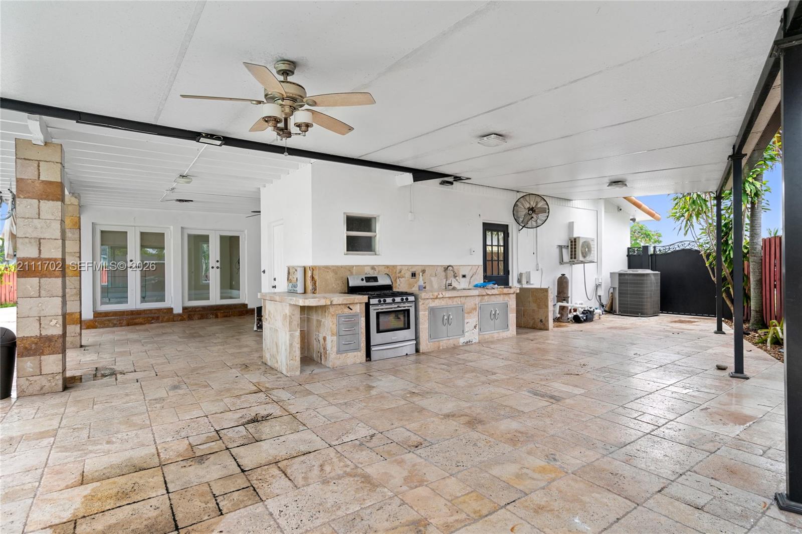 Covered patio featuring stone-tile flooring, outdoor kitchen with a built-in range and sink, ceiling fans, and structural stone pillars
