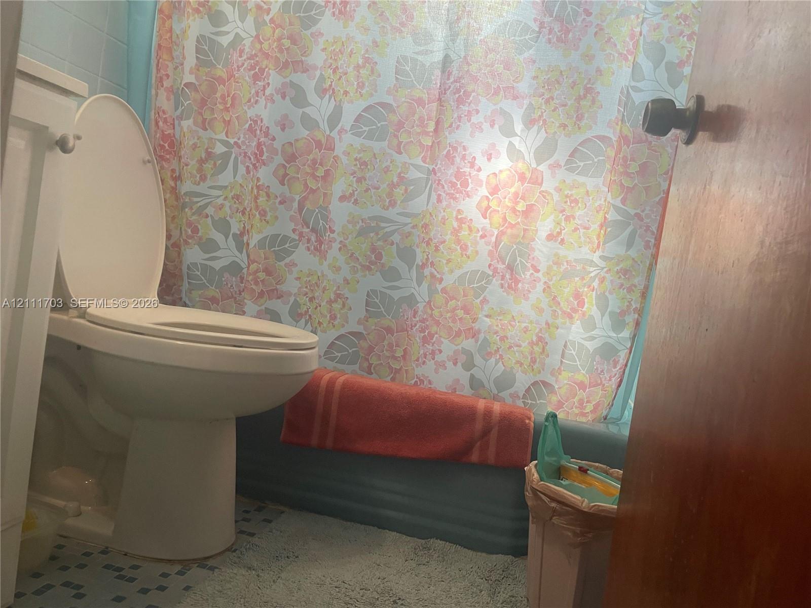 Bathroom featuring a standard toilet, a tub with a solid-color surround, and tiled flooring