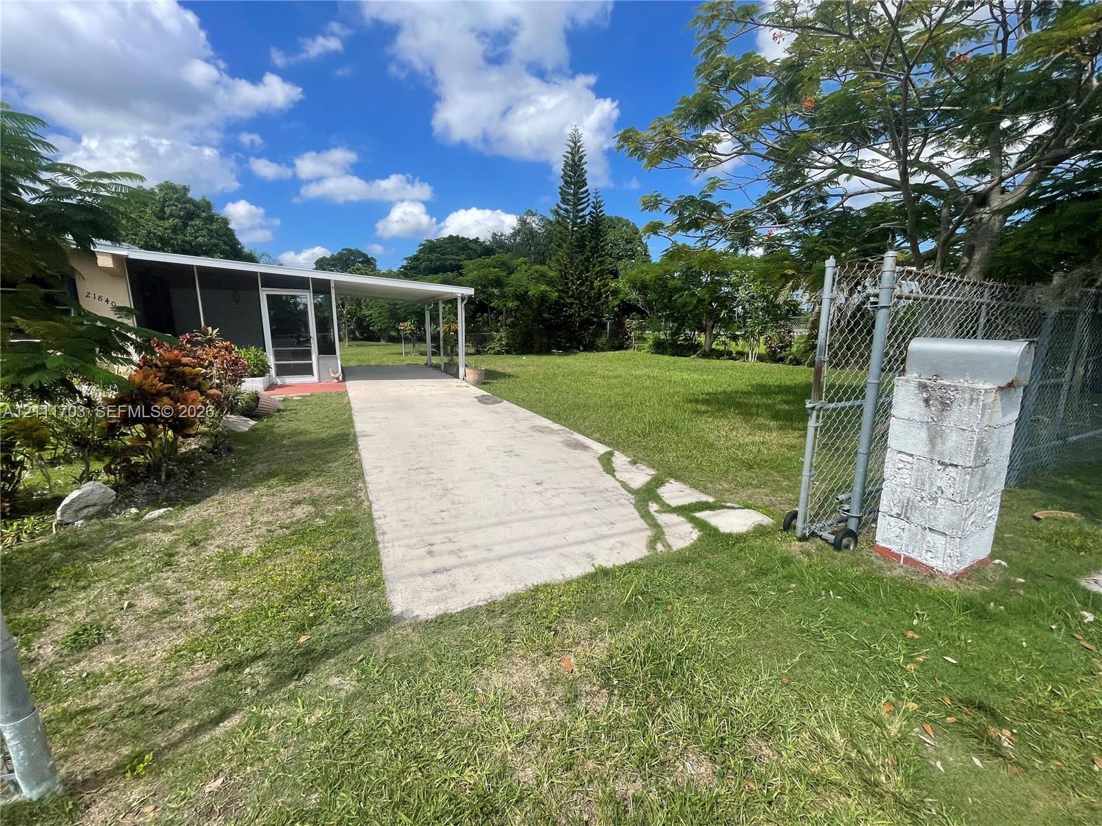 Expansive lot featuring a concrete driveway, covered patio, mature trees, and chain-link fencing Expansive lot featuring a concrete driveway, covered patio, mature trees, and chain-link fencing