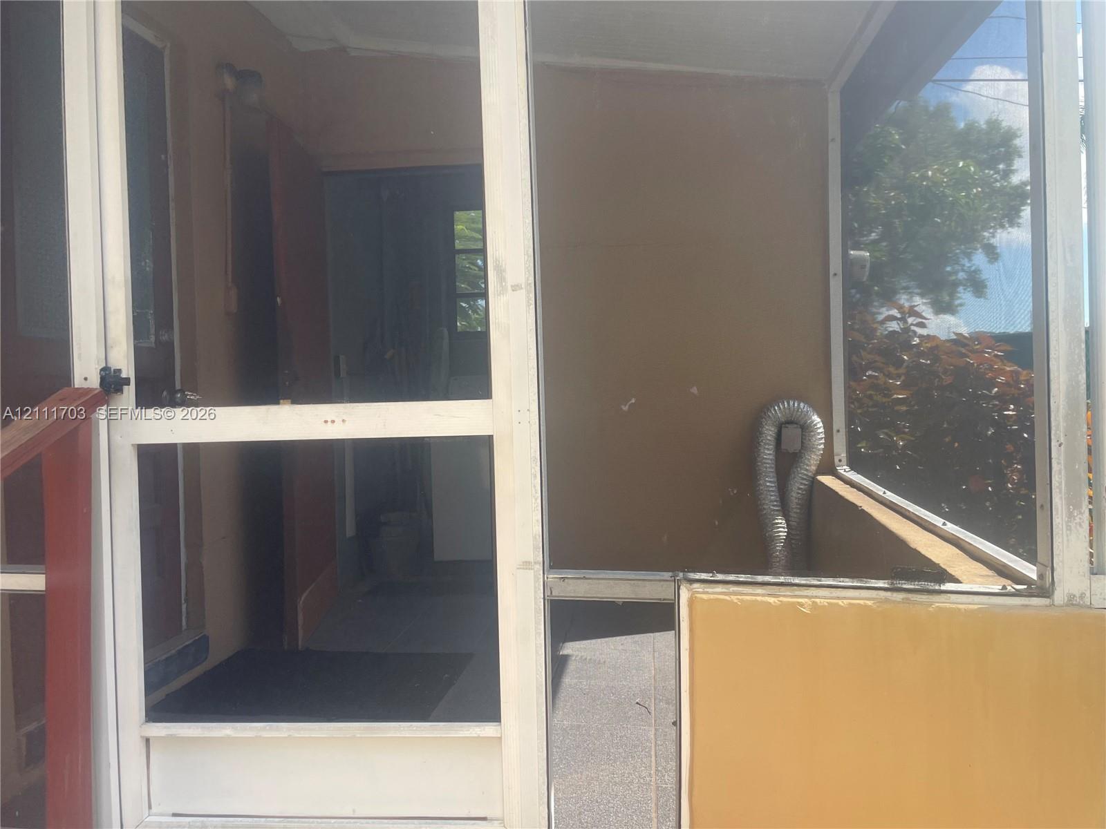 Screened porch featuring metal framing, solid lower wall panels, concrete flooring, and an integrated hinged screen door