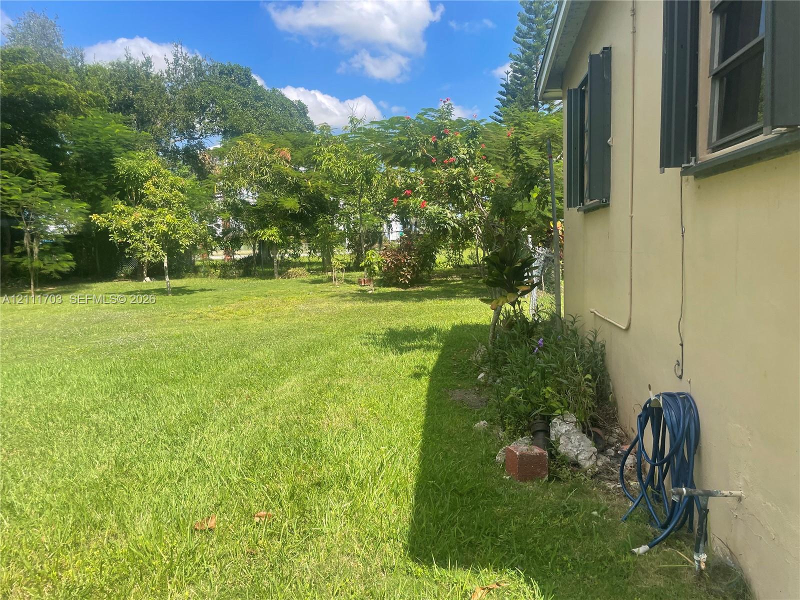 Expansive backyard featuring a large grass lawn, mature trees, and exterior wall-mounted shutters
