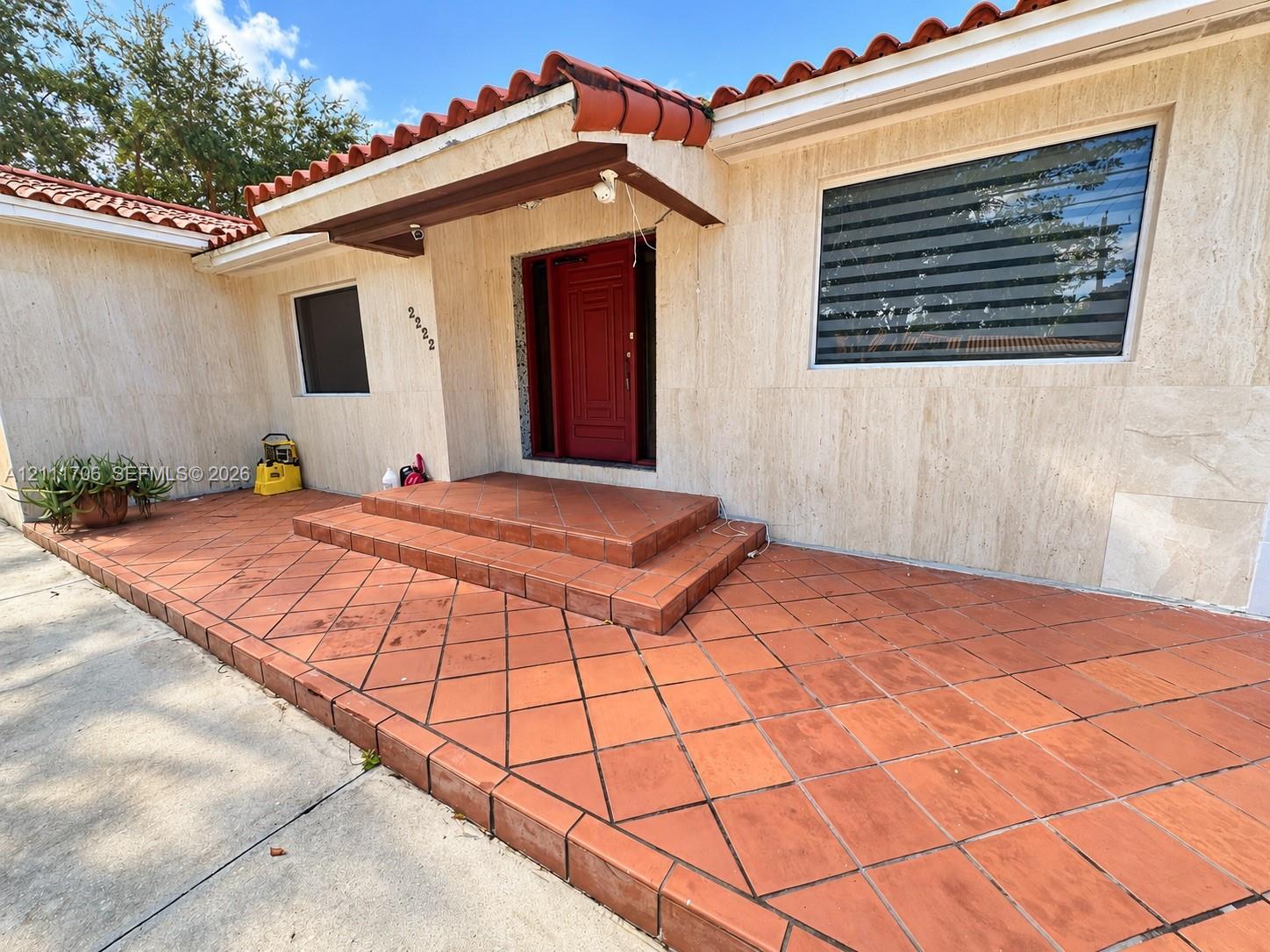 Exterior entrance featuring natural stone wall cladding, a terracotta tile porch, a low-profile overhang with a barrel-tile roof, and a solid-core entry door