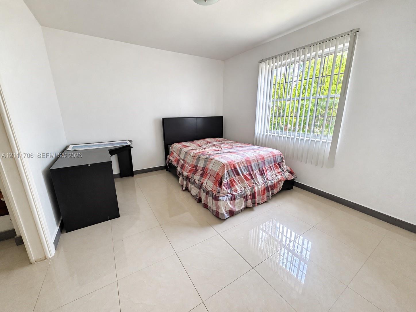 Neutral-toned tile flooring, white wall finishes, and a large window featuring vertical blinds